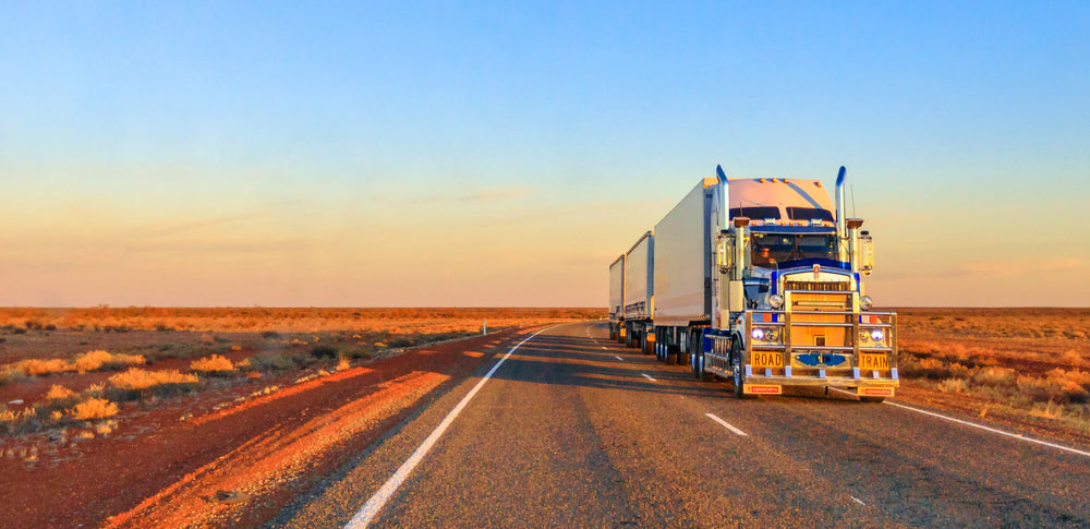 Road train travelling along an outback highway at sunset