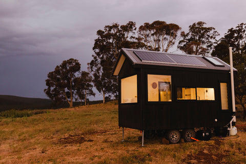 Tiny house on a trailer in a grassy field at dusk